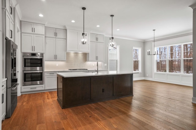 kitchen featuring tasteful backsplash, wood finished floors, stainless steel appliances, crown molding, and light countertops