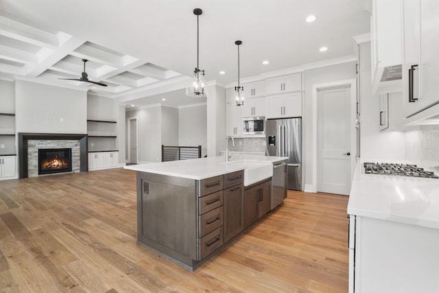 kitchen with stainless steel appliances, coffered ceiling, a sink, white cabinets, and light wood-type flooring