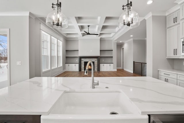 kitchen featuring a warm lit fireplace, coffered ceiling, open floor plan, wood finished floors, and a sink