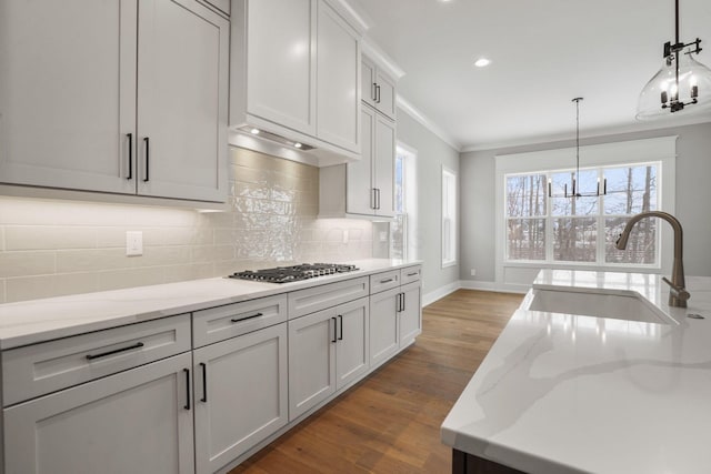 kitchen featuring stainless steel gas cooktop, wood finished floors, a sink, ornamental molding, and decorative backsplash