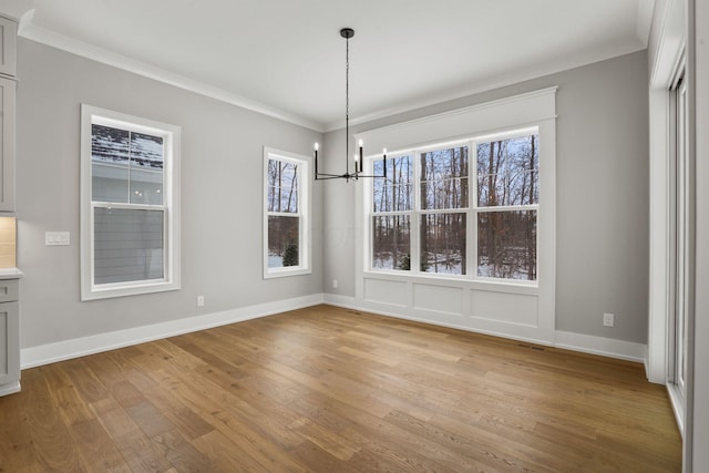 unfurnished dining area with a chandelier, ornamental molding, light wood-style flooring, and baseboards