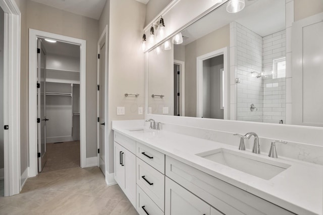 bathroom featuring double vanity, a walk in closet, a sink, and tiled shower