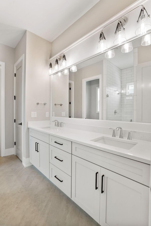 bathroom with a tile shower, double vanity, a sink, and baseboards