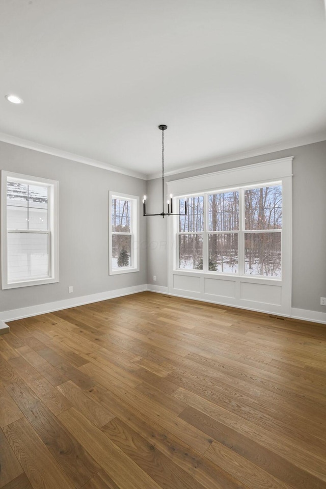 unfurnished dining area featuring crown molding, an inviting chandelier, wood finished floors, and baseboards