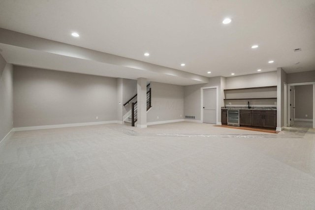 finished below grade area with light carpet, baseboards, wine cooler, stairway, and recessed lighting