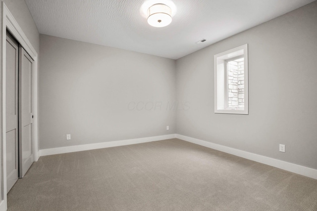 unfurnished bedroom featuring a textured ceiling, carpet floors, visible vents, baseboards, and a closet