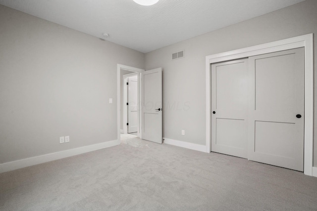 unfurnished bedroom featuring a textured ceiling, carpet floors, visible vents, baseboards, and a closet