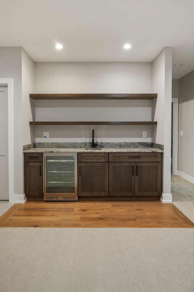 bar with beverage cooler, baseboards, light colored carpet, wet bar, and a sink