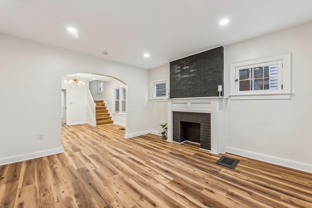 unfurnished living room featuring arched walkways, a fireplace, wood finished floors, visible vents, and stairway