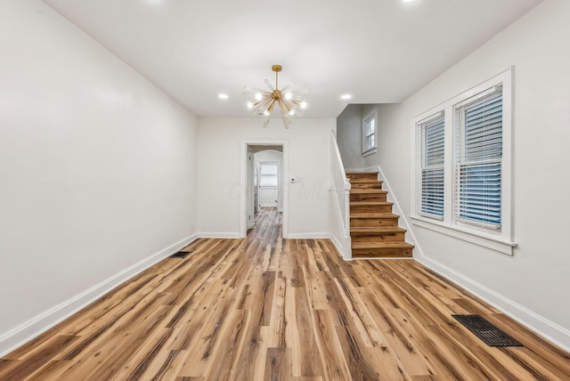 interior space with baseboards, visible vents, light wood-style flooring, an inviting chandelier, and stairs