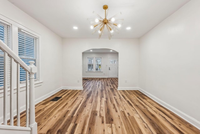 unfurnished living room with arched walkways, visible vents, an inviting chandelier, wood finished floors, and baseboards