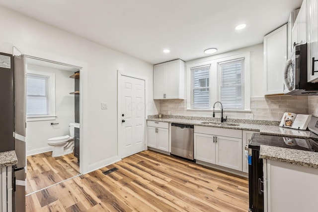 kitchen featuring light stone counters, a sink, stainless steel appliances, light wood-style floors, and backsplash