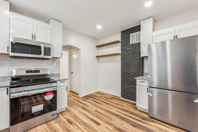 kitchen with arched walkways, appliances with stainless steel finishes, light wood-type flooring, backsplash, and open shelves