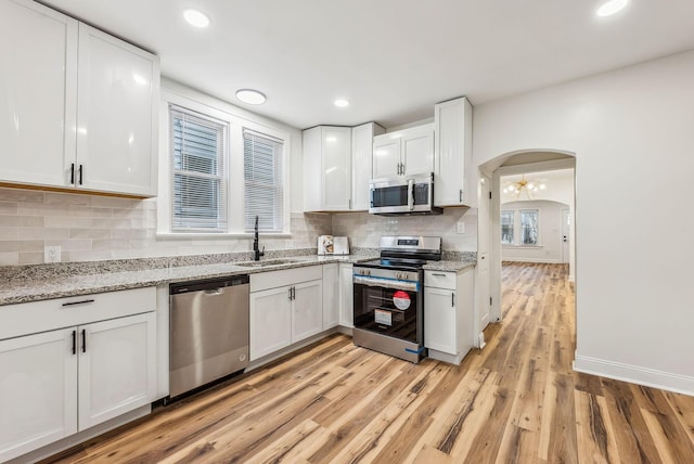 kitchen featuring white cabinets, appliances with stainless steel finishes, arched walkways, and a sink