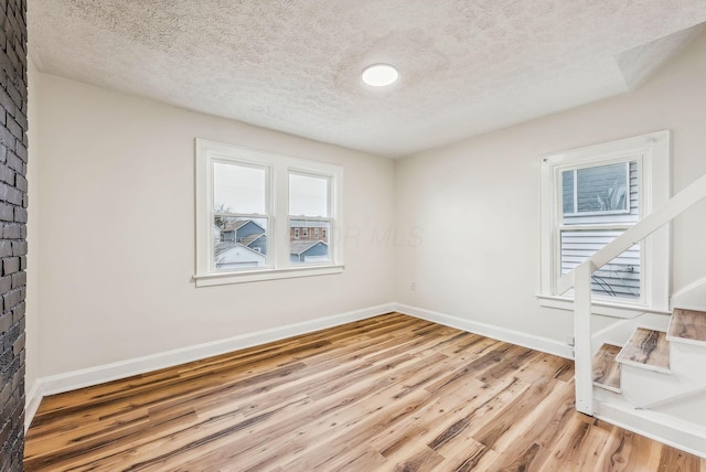 empty room with a textured ceiling, baseboards, and wood finished floors