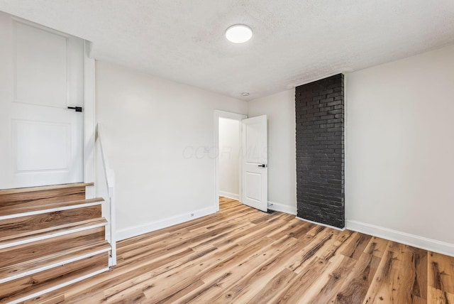 unfurnished room featuring light wood finished floors, stairs, baseboards, and a textured ceiling