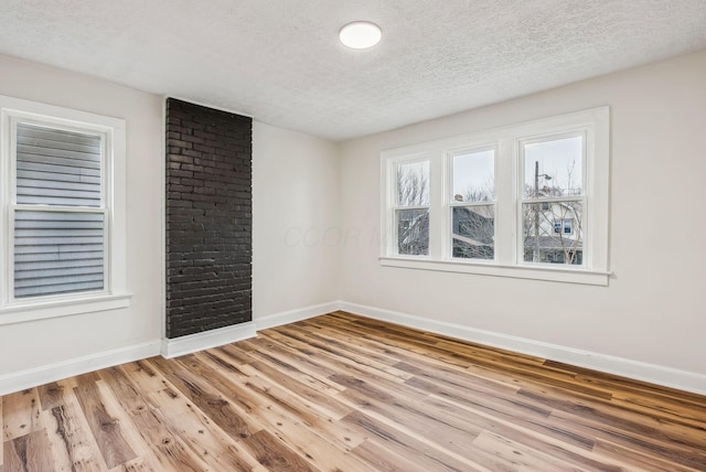 empty room featuring a textured ceiling, light wood-style flooring, and baseboards