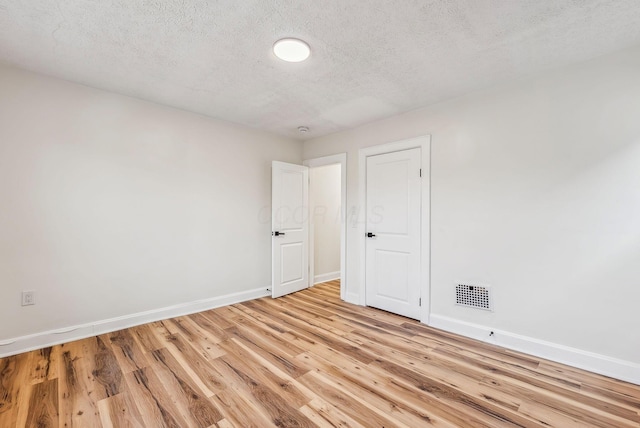 spare room featuring a textured ceiling, light wood-type flooring, visible vents, and baseboards