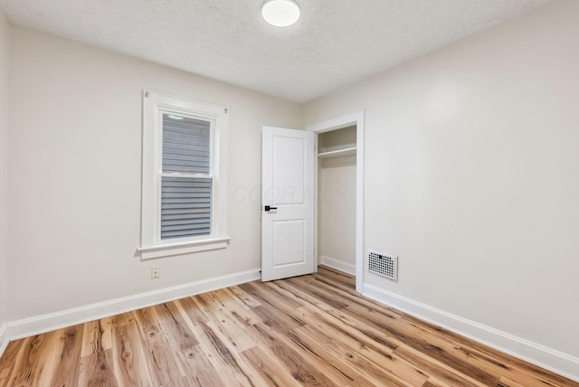 empty room with light wood-type flooring, visible vents, a textured ceiling, and baseboards