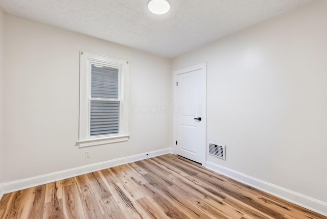 unfurnished room with baseboards, visible vents, a textured ceiling, and light wood finished floors