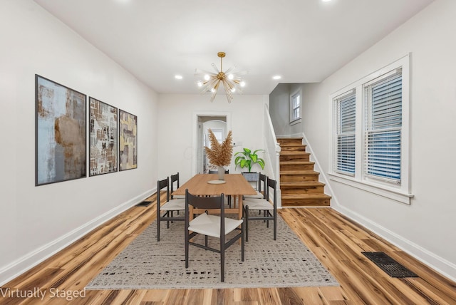 dining space featuring light wood finished floors, visible vents, a chandelier, baseboards, and stairs