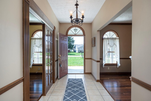 foyer entrance featuring light tile patterned floors, a textured ceiling, a healthy amount of sunlight, and a notable chandelier