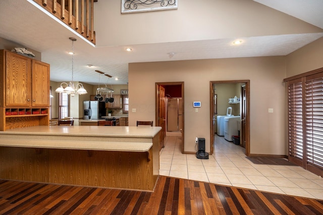 kitchen with light tile patterned floors, light countertops, a peninsula, stainless steel fridge with ice dispenser, and a notable chandelier