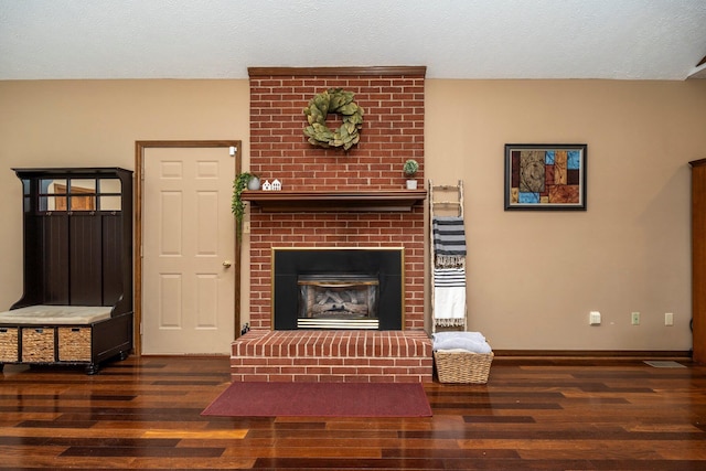 living area with baseboards, a textured ceiling, wood finished floors, and a brick fireplace