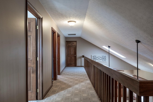 hall featuring a textured ceiling, an upstairs landing, visible vents, lofted ceiling with skylight, and light colored carpet