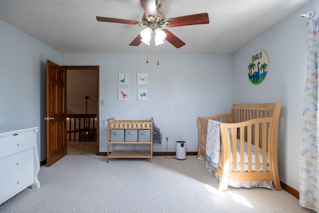 carpeted bedroom with a crib, baseboards, and ceiling fan