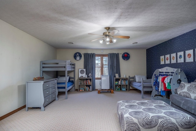 carpeted bedroom with a textured ceiling, baseboards, ceiling fan, wallpapered walls, and an accent wall