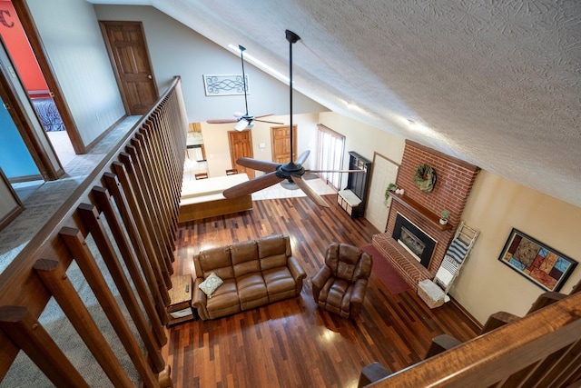living area featuring a ceiling fan, wood finished floors, a textured ceiling, a brick fireplace, and lofted ceiling