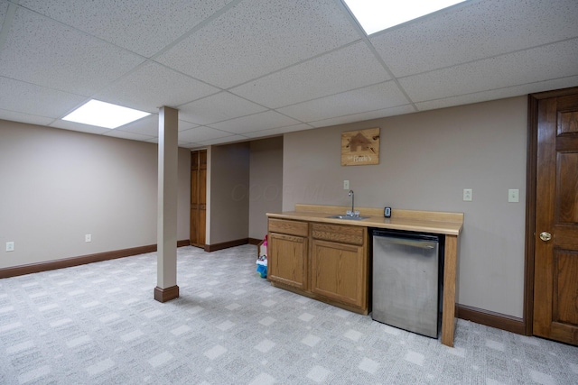 kitchen featuring a sink, fridge, brown cabinetry, baseboards, and a paneled ceiling