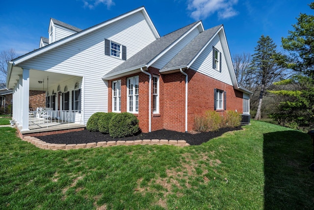 view of side of home featuring cooling unit, brick siding, a shingled roof, a porch, and a yard