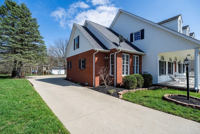 view of side of home with covered porch, a lawn, brick siding, driveway, and a shingled roof