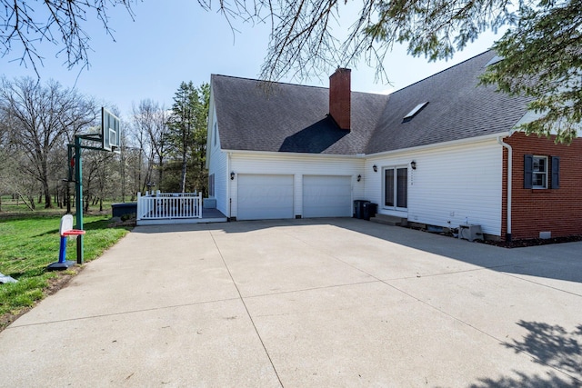 view of side of home with a chimney, a shingled roof, a garage, and concrete driveway