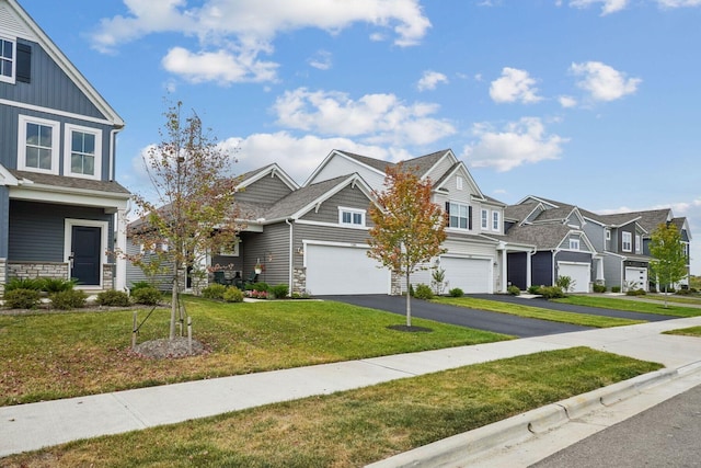 view of front of house featuring stone siding, a residential view, aphalt driveway, an attached garage, and a front yard