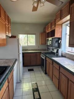 kitchen featuring black microwave, stainless steel range with gas stovetop, ceiling fan, and light tile patterned floors