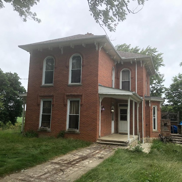 italianate-style house featuring covered porch, brick siding, and a front lawn