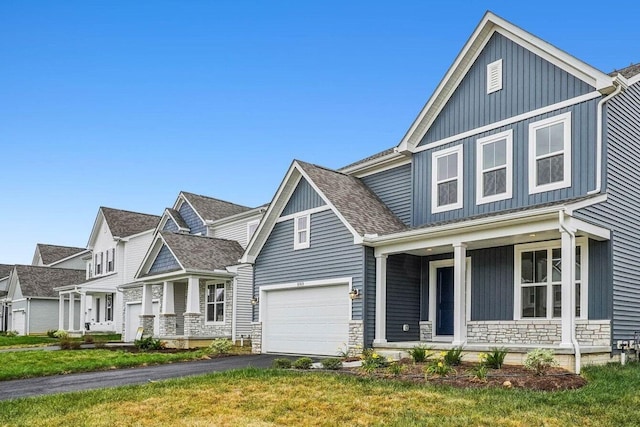 view of front of property featuring covered porch, board and batten siding, a garage, stone siding, and driveway