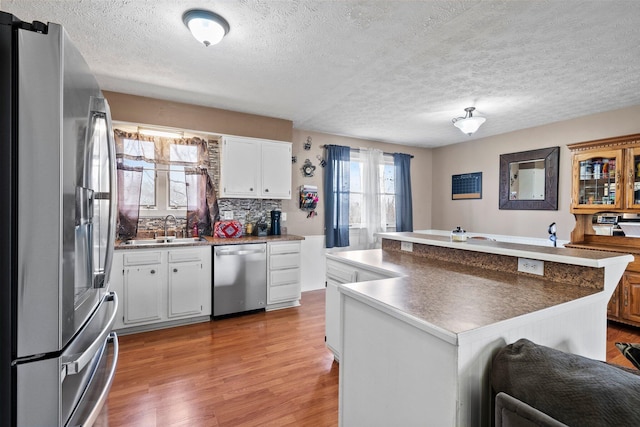 kitchen with a sink, white cabinetry, appliances with stainless steel finishes, light wood-type flooring, and backsplash