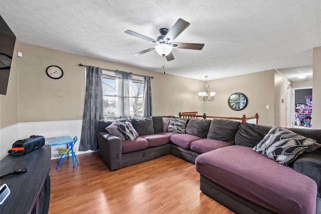 living area with a textured ceiling, ceiling fan with notable chandelier, wainscoting, and light wood-style flooring