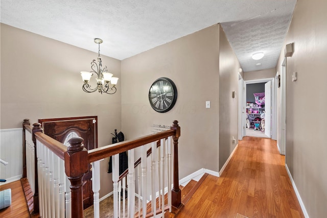 hallway featuring a notable chandelier, light wood-style floors, a textured ceiling, an upstairs landing, and baseboards