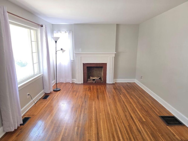 unfurnished living room with visible vents, baseboards, a fireplace with flush hearth, and hardwood / wood-style flooring