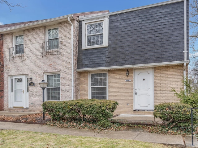 view of front of home featuring brick siding, mansard roof, and roof with shingles