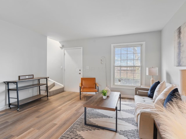 living area with baseboards, light wood finished floors, and stairs