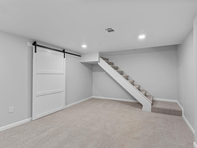 finished below grade area featuring carpet floors, visible vents, a barn door, baseboards, and stairs