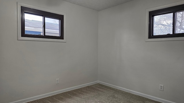 spare room with dark colored carpet, baseboards, and a textured ceiling