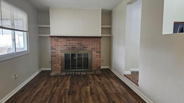 unfurnished living room featuring visible vents, a brick fireplace, baseboards, a textured ceiling, and dark wood-style flooring