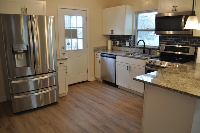 kitchen with white cabinets, stainless steel appliances, backsplash, wood finished floors, and a sink